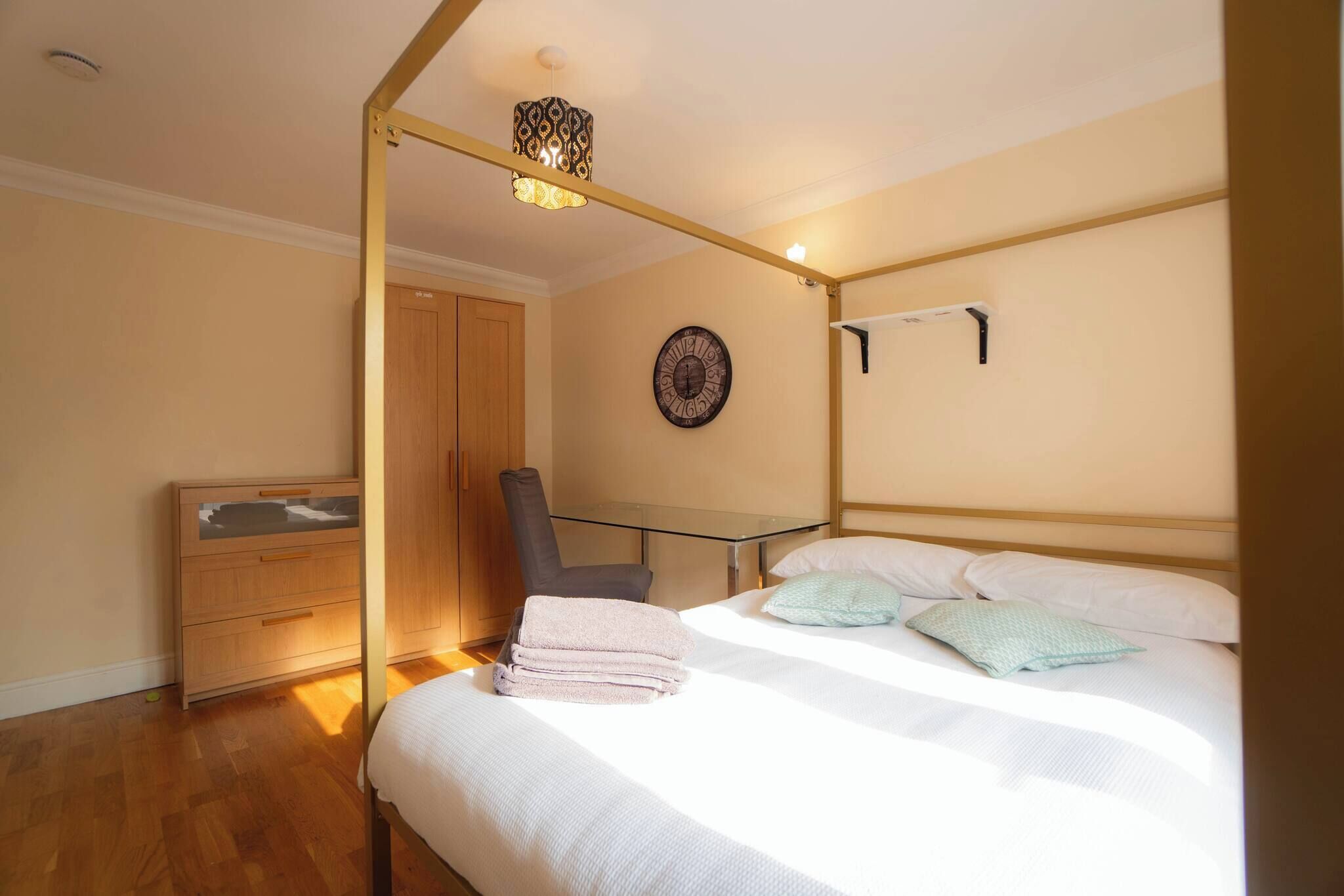 Un dormitorio con cama, una silla, un armario, un reloj y una lámpara colgante.