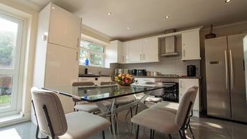A modern kitchen with a glass dining table, four chairs, stainless steel appliances, and a window with a view.