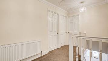 A hallway with two white doors, a white radiator, and a staircase with white balusters.
