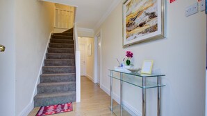 A staircase leading to a second floor, a glass console table with a vase and picture frame, and a painting on the wall. - Free Parking 7 Beds Contractor & Large Groups (Reading)
