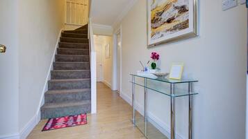 A staircase leading to a second floor, a glass console table with a vase and picture frame, and a painting on the wall.