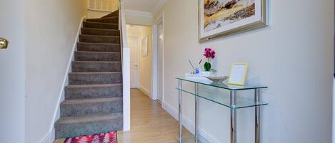 A staircase leading to a second floor, a glass console table with a vase and picture frame, and a painting on the wall.