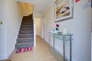 Eine Treppe führt zu einer zweiten Etage, ein Glastisch mit einer Vase und einem Bilderrahmen, und ein Gemälde an der Wand.