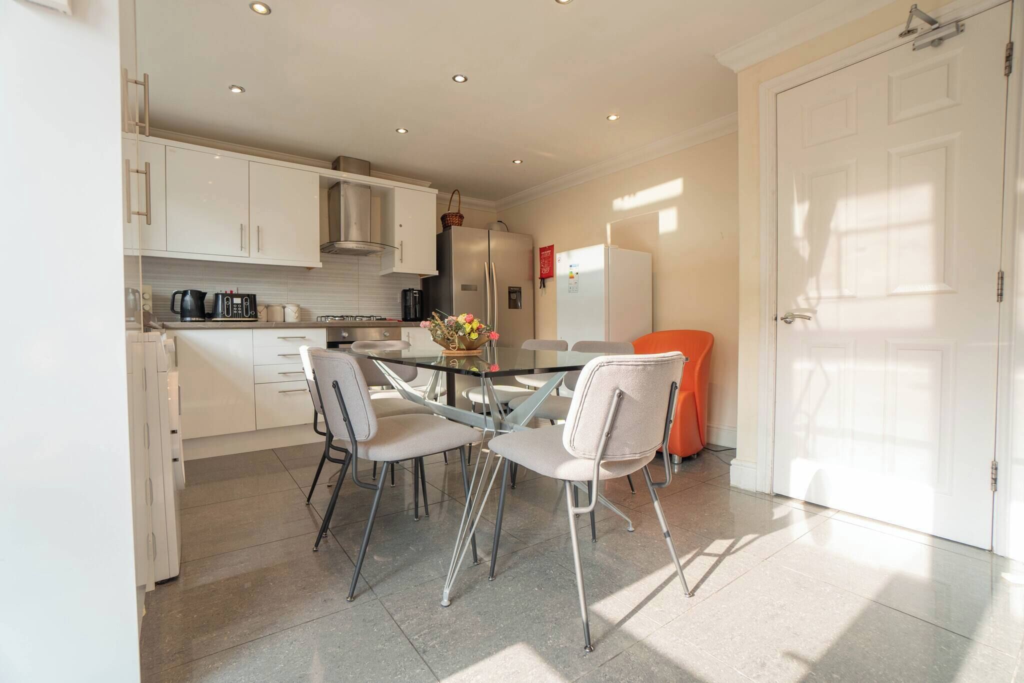 A modern kitchen with white cabinets, a stainless steel refrigerator, and a dining table with four chairs.