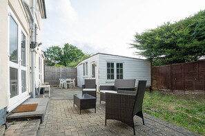 Eine Terrasse mit Gartenmöbeln, einem kleinen Gartenhaus und einem Holzzaun.