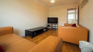 A living room with a flat-screen TV, a black entertainment unit, and two orange sofas. - Free Parking 7 Beds Contractor & Large Groups (Reading)