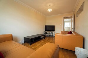 Ein Wohnzimmer mit einem Flachbildfernseher, einer schwarzen Unterhaltungseinheit und zwei orangenen Sofas.