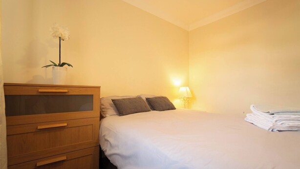 A hotel room with a bed, a wooden dresser, a nightstand with a lamp, and a plant. - Free Parking 7 Beds Contractor & Large Groups (Reading)