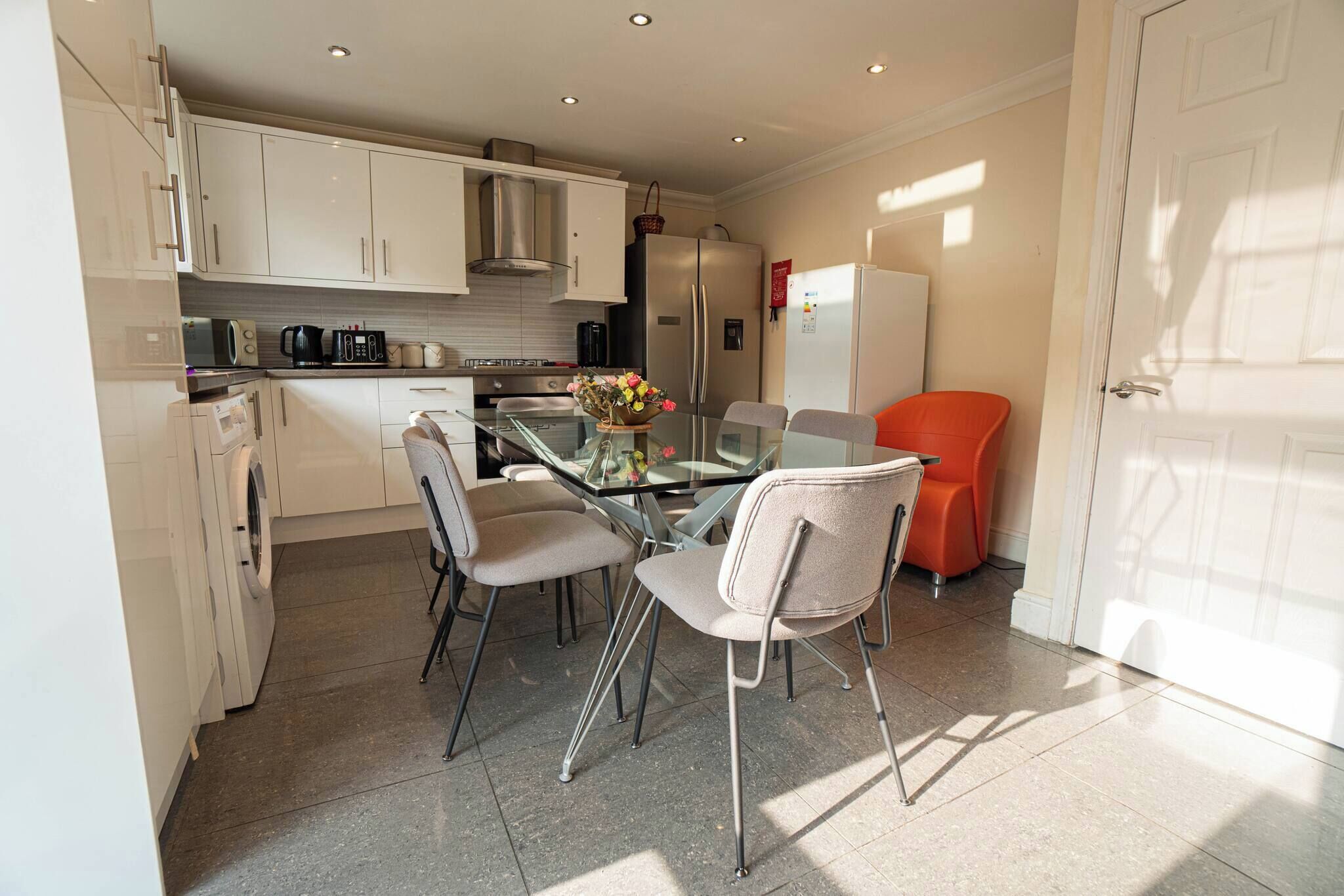 A compact kitchen with white cabinets, a glass dining table, and two chairs.