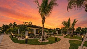 Un resort con un camino pavimentado, palmeras y un edificio con ventanas grandes.