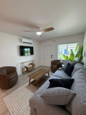 Ein Wohnzimmer mit einer Couch, zwei Sesseln, einem Couchtisch, einem Fernseher und einem Deckenventilator.