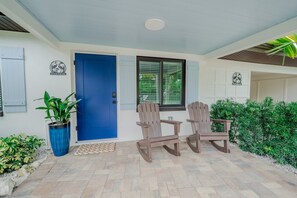 A front porch with a blue door, two wooden chairs, a potted plant, and a small table. - 18 On the Bay Suite #1 (Indian Rocks Beach)