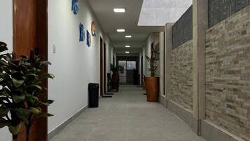 Un pasillo con una puerta de madera, una planta en maceta y un basurero.