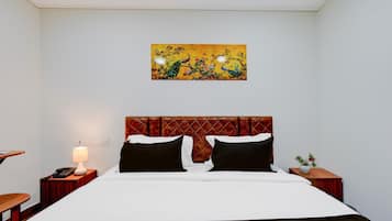 Habitación de hotel con una cama, una mesita de noche con lámpara, un cuadro en la pared y una pequeña mesa con una planta.