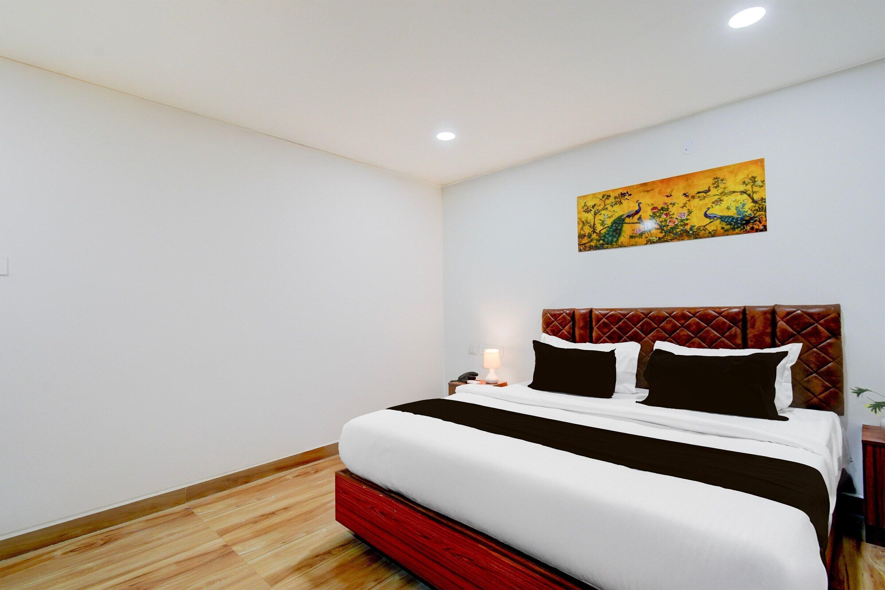 A hotel room with a bed, a nightstand, a lamp, and a painting on the wall.