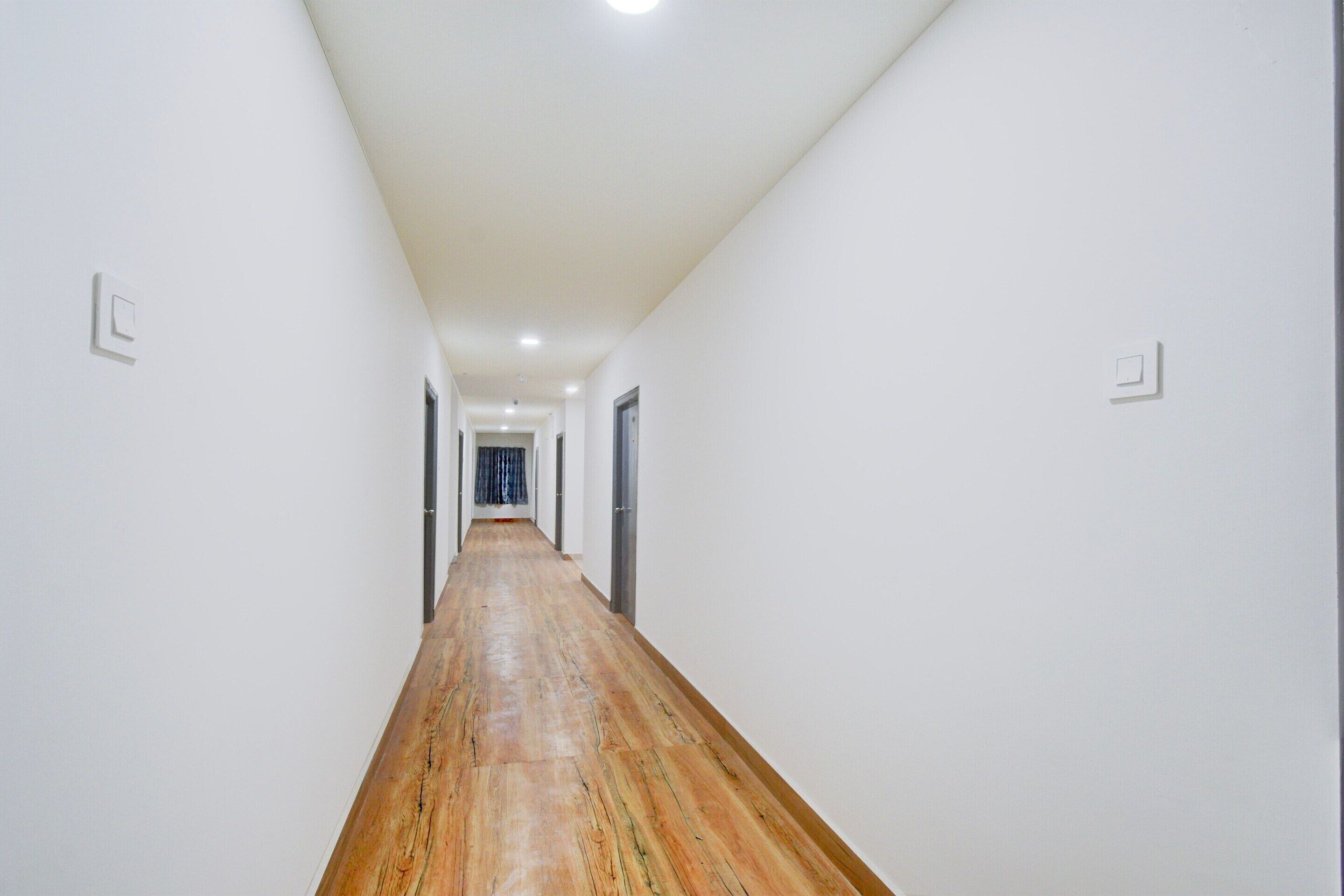Un pasillo con paredes blancas y piso de madera, que lleva a una puerta al final.