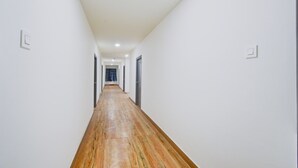 A corridor with white walls and wooden flooring, leading to a door at the end. - Premium Vanasthalipuram Near (Hyderabad)