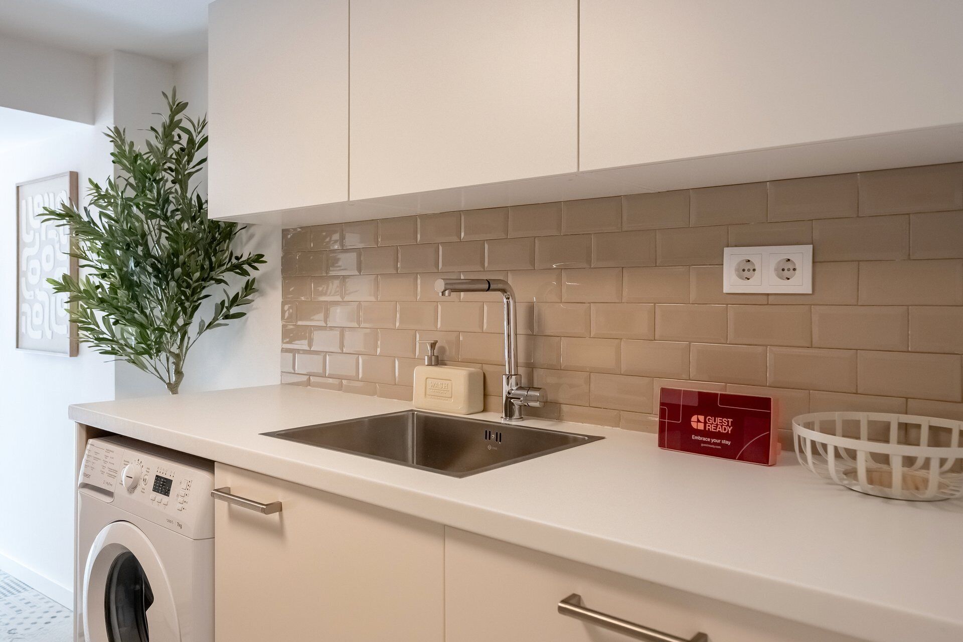 A modern kitchen with a built-in sink, a washing machine, and a decorative plant.