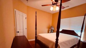 Quarto com cama de dossel, ventilador de teto e janela com persianas.
