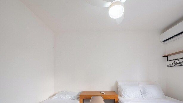 Een simpele, nette kamer met twee bedden, een klein houten bureau, een stoel en een wandairconditioner.