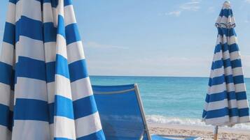 Escena de playa con una silla y dos sombrillas a rayas.