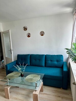 A teal sofa, a glass coffee table with a woven placemat, and a wall with three decorative plates. - Chmielna 3-bedroom apartment in City Center,Pet Friendly (Warszawa)