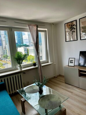 A modern living room with a glass coffee table, a radiator, a window with curtains, a TV on a stand, and framed artwork on the wall. - Chmielna 3-bedroom apartment in City Center,Pet Friendly (Warszawa)