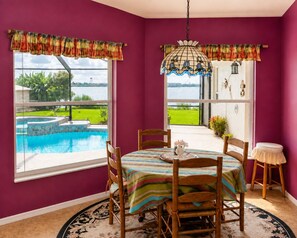 Une pièce avec vue sur une piscine, une table à manger avec des chaises, un luminaire suspendu et un petit tabouret.