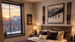 A bedroom with a large window, a bed with a plaid blanket, a ski-themed wall art, and a sign that says 'SKI IDAHO'. - Dream Ski Chalet. Views. Ski-in Ski-out, hot tub, directly on ski run. #1 (Sandpoint)