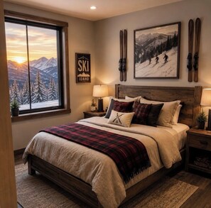 Ein Schlafzimmer mit großem Fenster, einem Bett mit kariertem Überwurf, Wandkunst zum Thema Skifahren und einem Schild mit der Aufschrift 'SKI IDAHO'.