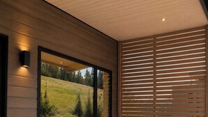 A modern spa area with a hot tub, wooden steps, and a large window offering a view of a green landscape. - Dream Ski Chalet. Views. Ski-in Ski-out, hot tub, directly on ski run. #1 (Sandpoint)