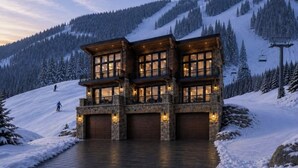 A multi-story lodge with large windows and stone walls, set against a snowy mountain backdrop. - Dream Ski Chalet. Views. Ski-in Ski-out, hot tub, directly on ski run. #1 (Sandpoint)