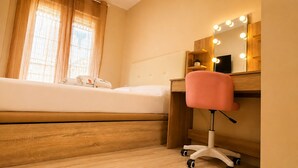 Ein Schlafzimmer mit einem Bett, einem Schreibtisch mit Stuhl, einem Schminktisch mit Beleuchtung und einem Fenster mit Vorhängen.