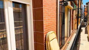 Eine schmale Stadtgasse mit einem Backsteingebäude, einem Metallgitter und einem gelben Stuhl, der an die Wand gelehnt ist.