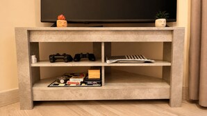 Ein Betonschrank für den Fernseher mit Spielcontrollern, einem Brettspiel und einer Pflanze.