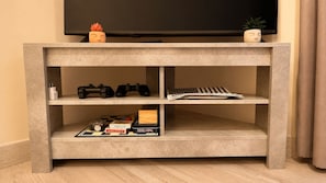 Ein Betonschrank für den Fernseher mit Spielcontrollern, einem Brettspiel und einer Pflanze.