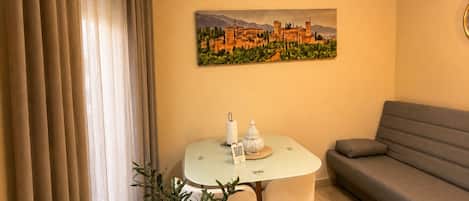 Una habitación con una mesa redonda, un sofá, un cuadro de un castillo y una cortina.