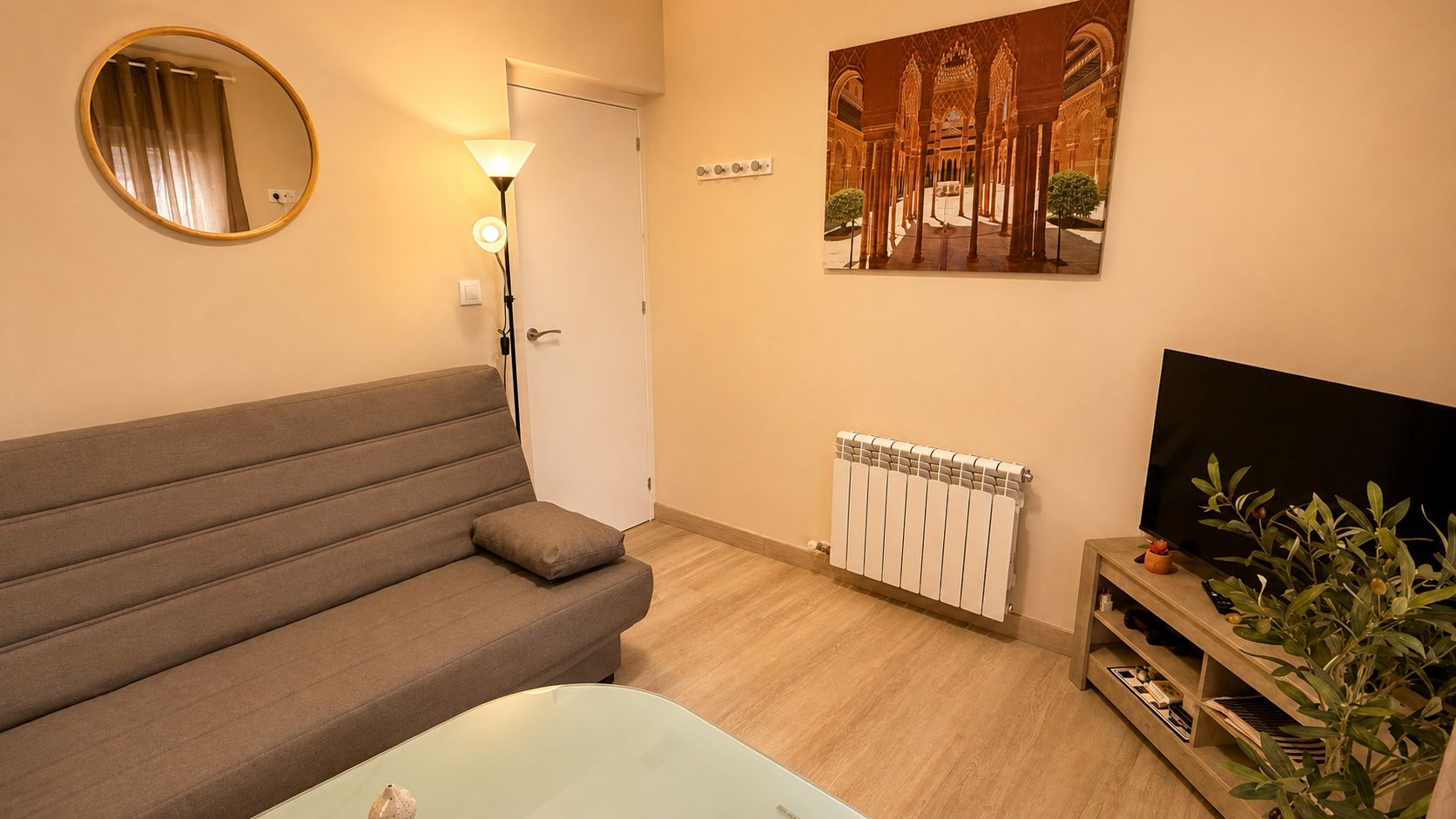 A living room with a sofa, a floor lamp, a radiator, a television, and a painting on the wall.