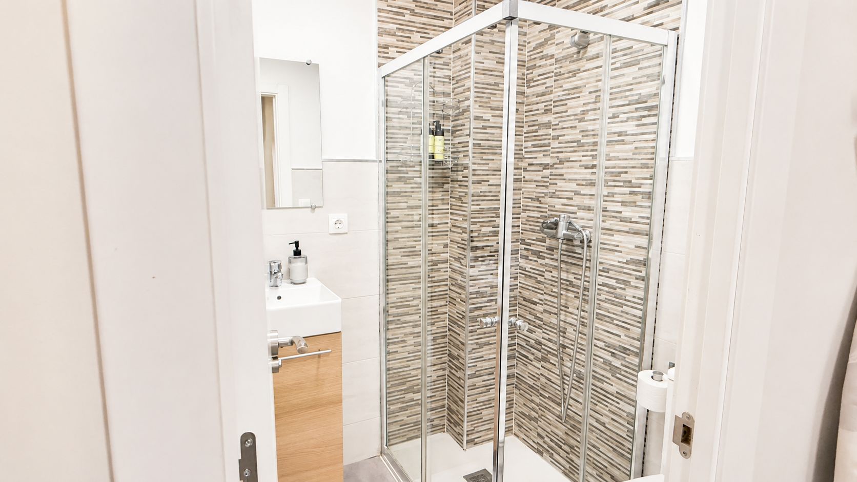 Un bagno moderno con box doccia in vetro, lavandino bianco e specchio.