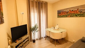 Ein Wohnzimmer mit Flachbildfernseher, einem Esstisch mit Stühlen, einer Topfpflanze und einem Gemälde an der Wand.