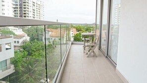 Ein Balkon mit Glasgeländer, einem Tisch und Stühlen sowie Blick auf Gebäude und Grünflächen.