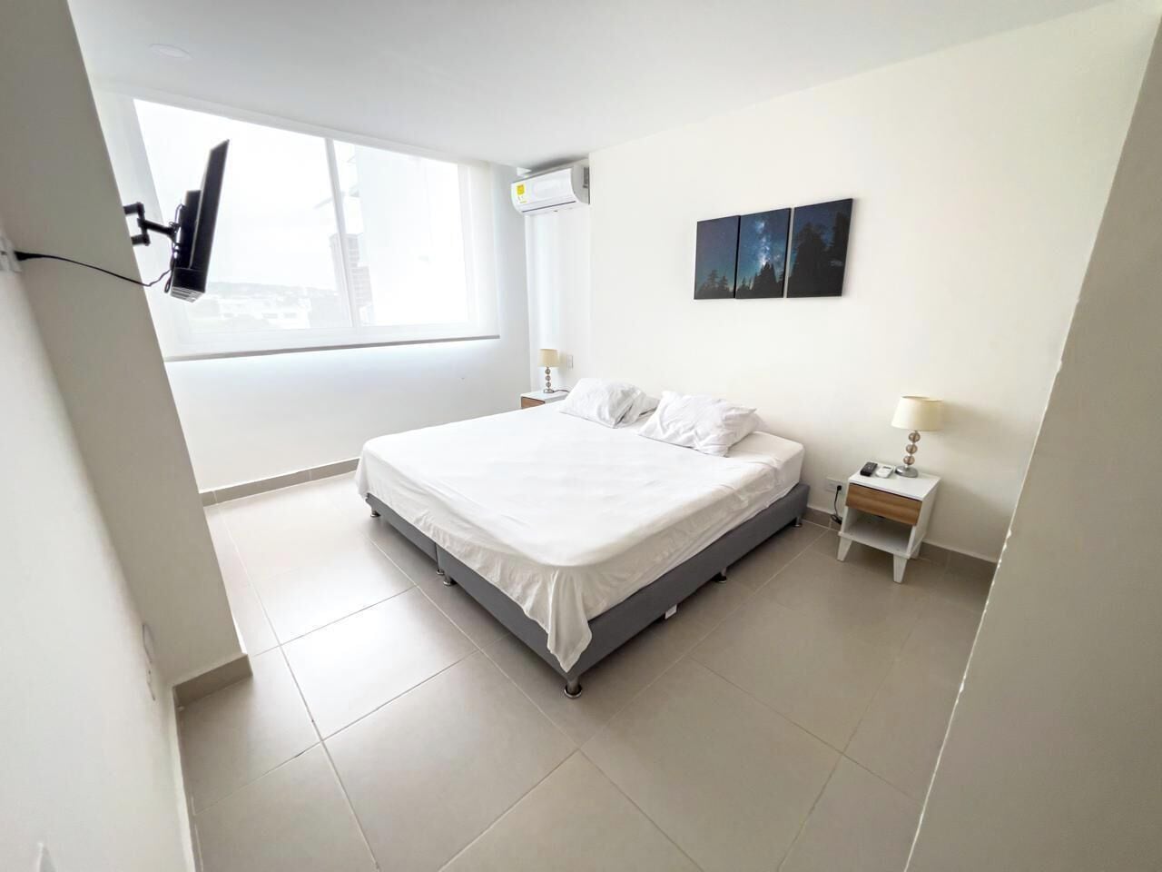 Une chambre à coucher comprenant un lit, une table de chevet, une lampe et un téléviseur fixé au mur.