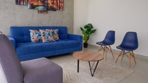 Ein Wohnzimmer mit einem blauen Sofa, zwei blauen Sesseln, einem runden Holztisch und einer Topfpflanze.