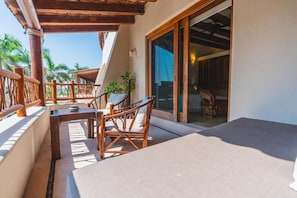 A balcony with a table and chairs, a sliding glass door leading to an interior room, and a view of palm trees.