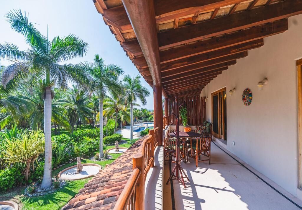 Un patio al aire libre con mobiliario de madera, rodeado de exuberante follaje y palmeras.