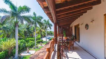 Un patio al aire libre con mobiliario de madera, rodeado de exuberante follaje y palmeras.