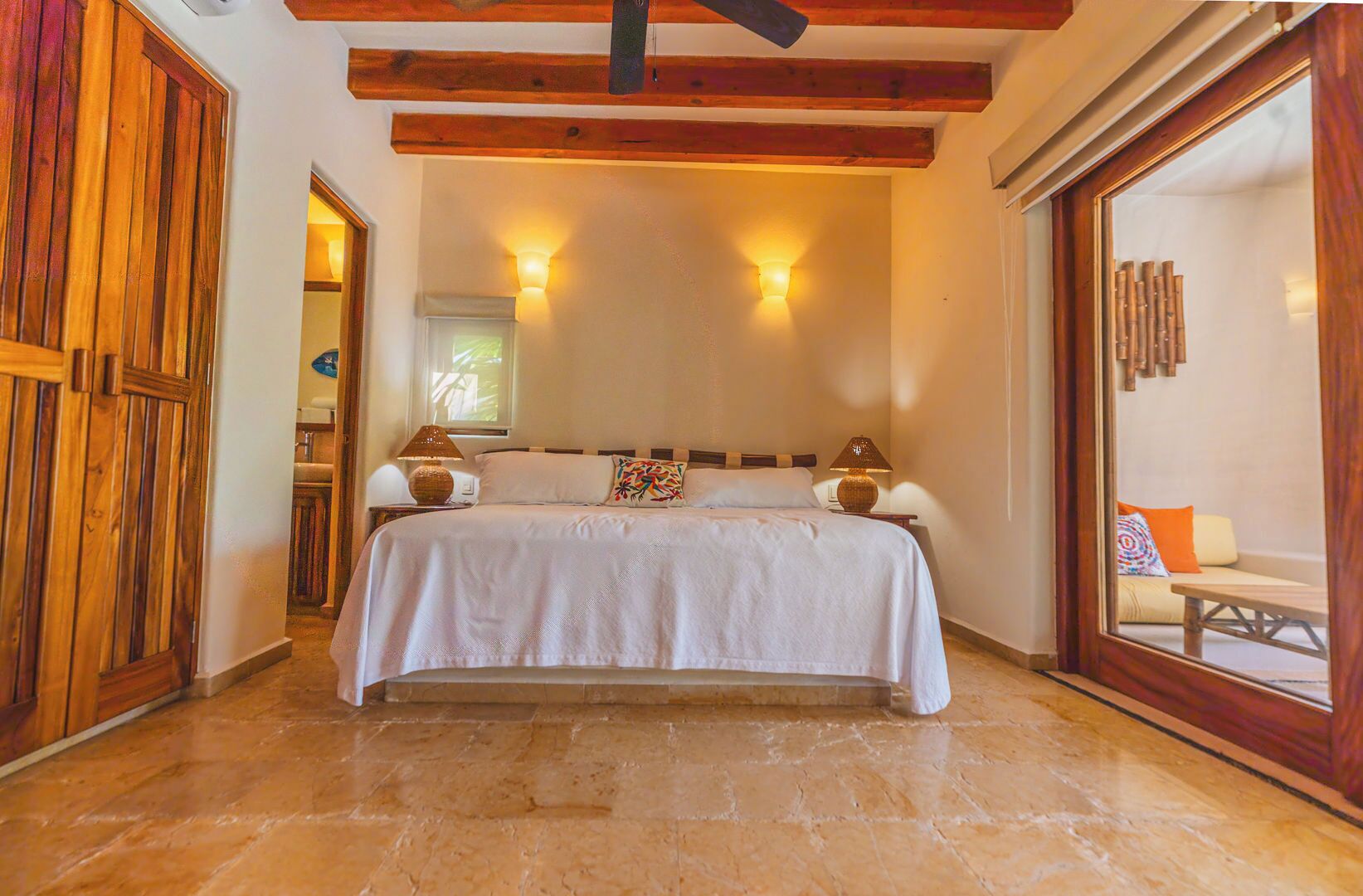 A bedroom with a bed, two bedside lamps, a wooden ceiling, and a large window.