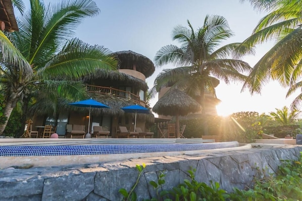 Un resort con piscina, construcciones de techo de paja y palmeras.