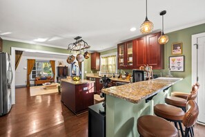 A modern kitchen with a central island, wooden cabinets, and pendant lighting. - Escape to the Arts, Golf Sim, Theater, Hot Tub (Charlotte)