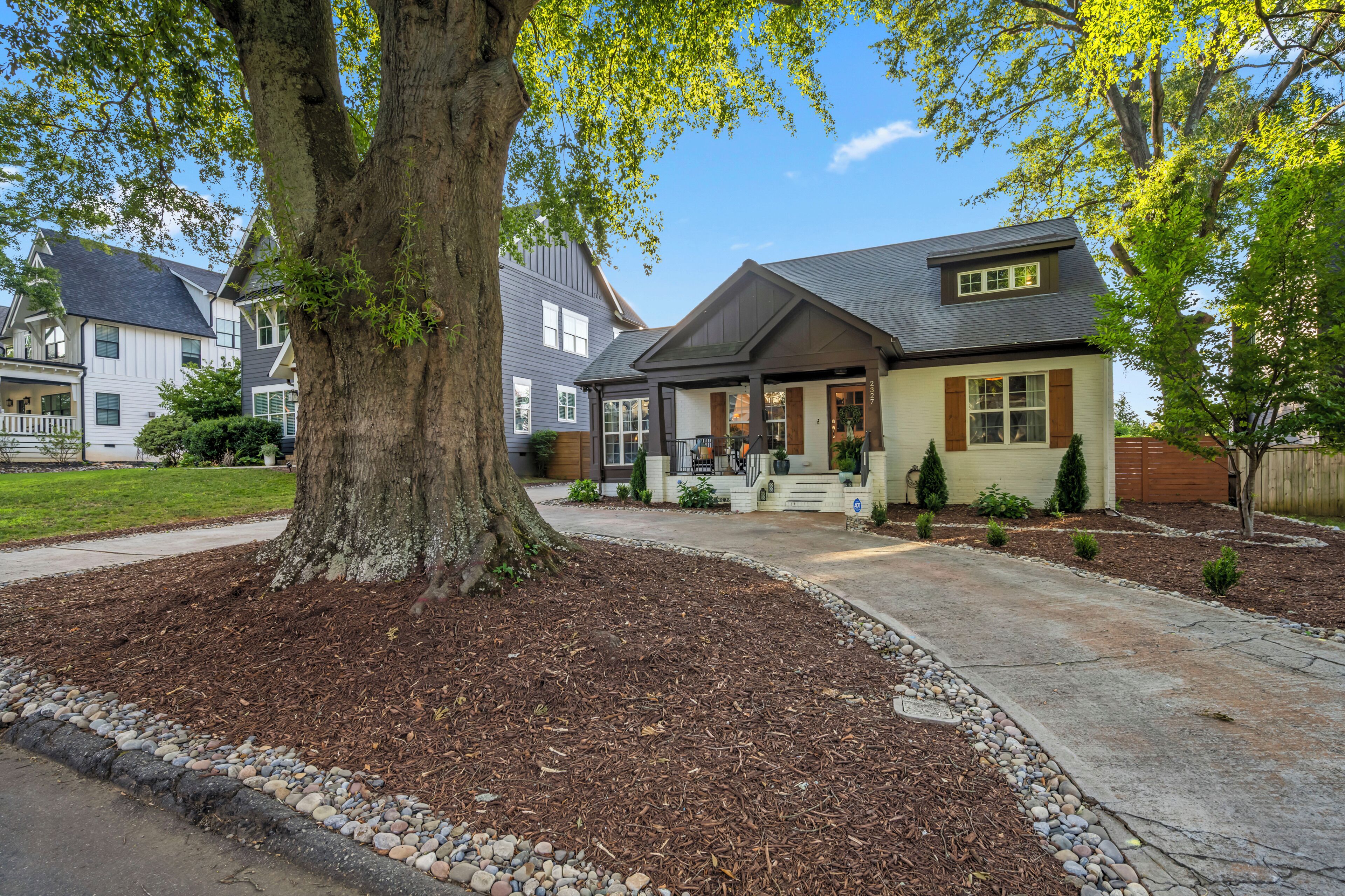A residential house with a large tree in the front yard, a well-maintained lawn, and a driveway leading to the entrance.
